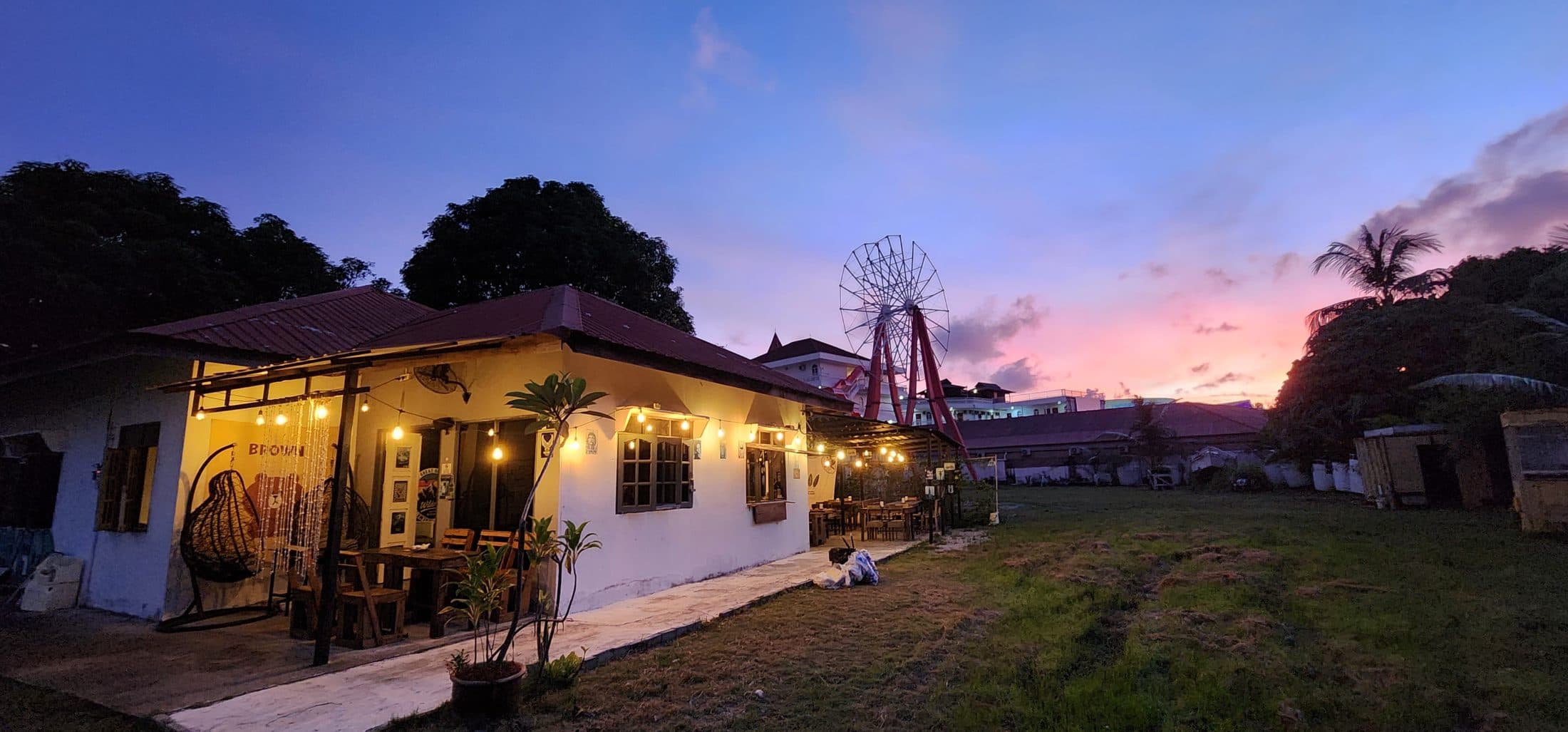 Brian's Bar at dusk — the bungalow glowing under string lights, old ferris wheel behind